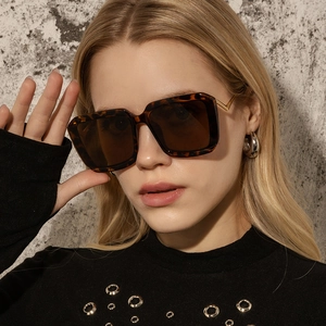 Close-up of tortoise square sunglasses with gold metal temples worn by a model