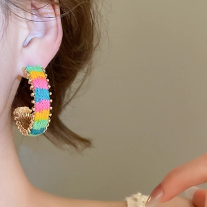 Detail of a C-shaped woven earring featuring colorful threads and gold bead edging