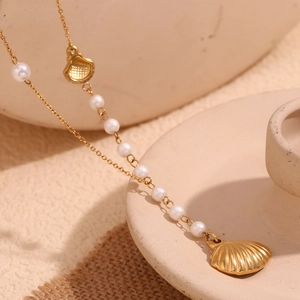 Close-up of a gold-plated shell pendant necklace with a white pearl on a ceramic stand