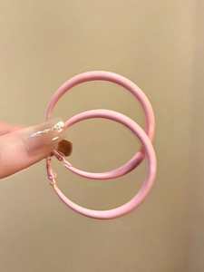 Detail view of large pink enamel hoop earrings being held to show scale and color