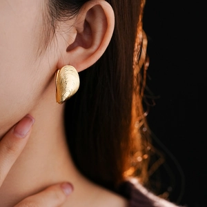 Close-up of a gold seashell-shaped screw thread earring worn by a model in soft light