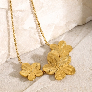 Detailed macro shot of three gold flower pendants on a textured stainless steel necklace