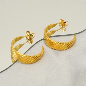 Macro detail of gold U-shaped earrings with spiral relief pattern on a mirror surface