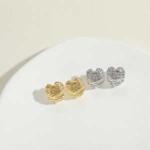 Minimalist textured heart stud earrings in gold and silver finish on ceramic tray