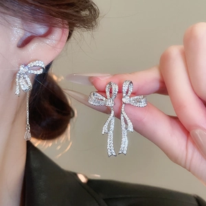 Close-up of asymmetric bow earrings with silver tassels and white zircon pavé