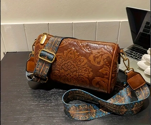 Detail of vintage brown cylinder bag with embossed floral pattern and retro wide strap