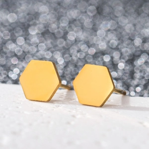 Macro shot of minimalist gold hexagonal stud earrings on a textured white stone base