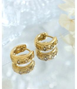 Détail de boucles d'oreilles en titane doré avec motifs d'étoiles et d'yeux et zircons blancs