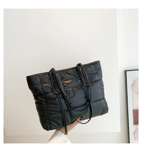 Detail of black quilted down tote bag featuring square padding and slim shoulder straps