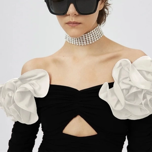 Detail of elegant off-shoulder top featuring large 3D white floral ruffles and chest cutout