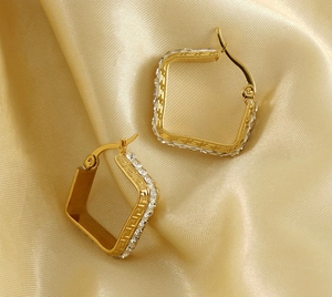 Detail of square gold-plated earrings with side zircons on soft silk background
