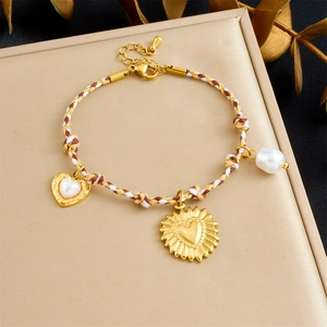 Detail of woven rope bracelet with gold heart charms and pearl on a golden stand