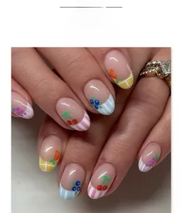 Close-up of short oval press-on nails with cartoon fruit patterns and French tips