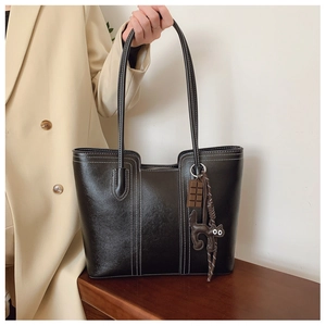 Detail of black faux leather tote bag with cat charm and high-quality stitching texture