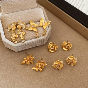 Macro view of matte 24K gold plated flower and butterfly earrings with cubic zirconia