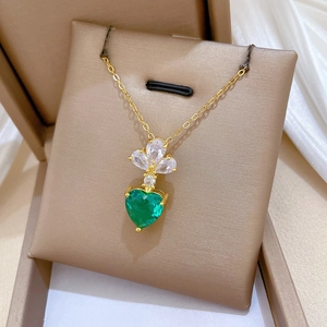 Macro shot of gold heart necklace with green crystal and zircon in a beige jewelry box