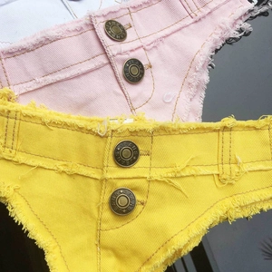 Dettaglio di pantaloncini di denim con frange e bottoni metallici gialli e rosa