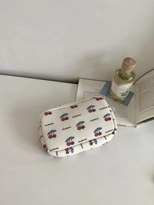 Detail of cherry print canvas makeup bag with Les Grenadas text on white desk