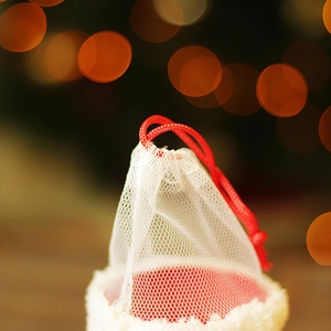 Sac cadeau de Noël en résille avec cordon rouge et bordure peluche sur fond bokeh