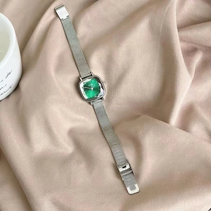 Detail of square green dial watch with silver mesh strap on warm fabric background