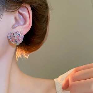 Close-up of sparkling heart-shaped pink multi-colored stud earring on female model's ear