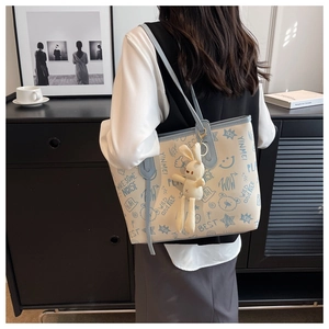 Detail of a large graffiti tote bag with a white plush bunny charm on a blue handle