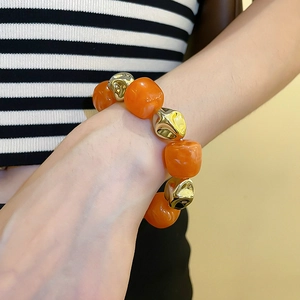 Detail of orange translucent acrylic beads and irregular golden metal spheres on a bracelet