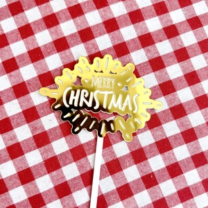 Close-up of golden mirror acrylic Merry Christmas cake topper on red checkered cloth