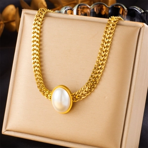 Detailed close-up of a large oval pearl pendant on a gold braided link necklace chain