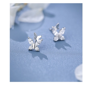 Macro shot of silver butterfly stud earrings with sparkling cubic zirconia on blue surface