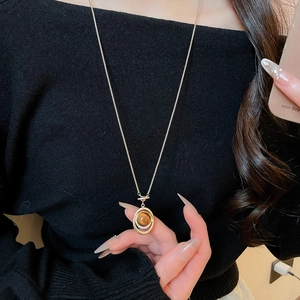 Detail of tiger eye stone pendant necklace on black knit sweater for autumn style