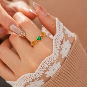 Détail d'une bague vintage plaquée or avec cœur vert et texture tressée sur le doigt
