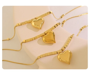 Macro view of gold snake chain necklaces with polished puffy heart pendants on white props