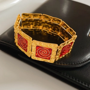 Detailed view of vintage gold-tone bracelet with red enamel spiral patterns on black leather