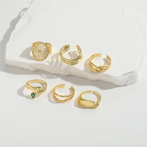 Macro view of six gold-plated fashion rings featuring green teardrop gems and intricate mesh patterns