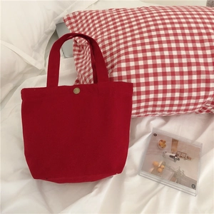 Detailed close-up of a red canvas lunch bag featuring a brass metal snap fastener on a bed