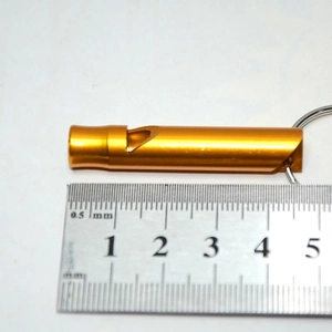 Golden aluminum emergency survival whistle with keychain loop shown against a measuring ruler