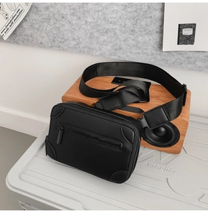 Detail of a black matte leather crossbody box bag with wide nylon strap and dual zippers