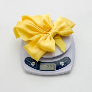 Detailed top view of a yellow satin bow hair clip on a digital scale showing weight