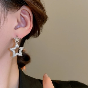 Macro detail of silver star drop earrings featuring crystal pavé on a woman's ear