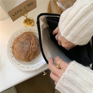 Close-up of a black and white canvas cat pouch being opened by hand with jewelry