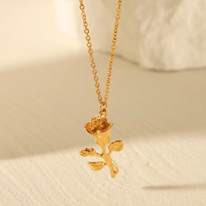 Detailed view of a gold rose pendant necklace hanging over a beige textured background