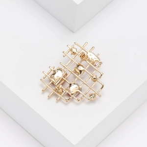 Close-up of golden hollow heart brooch with rhinestone grid pattern on white podium