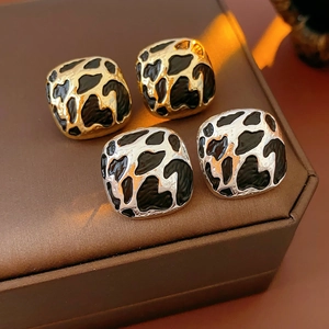 Détail macro de boucles d'oreilles carrées léopard en finitions noir-or et noir-argent
