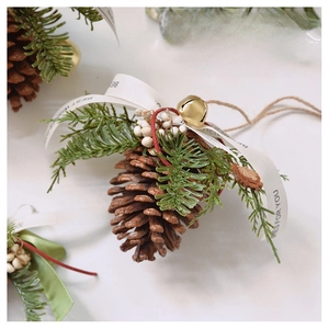 Macro shot of natural pine cone ornament with gold bells and printed ribbons on marble