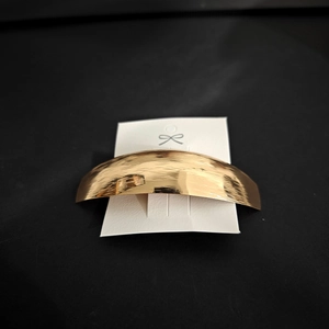 Close-up of golden metal barrette with brushed texture on white card display