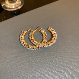 Detail view of C-shaped golden earrings with sparkling diamonds on grey textured surface