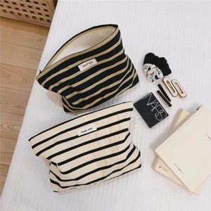 Flat lay of striped cotton toiletry bags in black-white and brown-black on cozy bedding