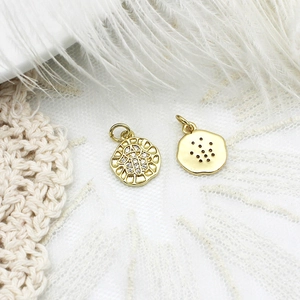 Macro shot of gold Hamsa hand and textured round charms on delicate white lace and feathers