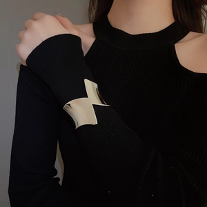 Dettaglio di un ampio bracciale rigido argento lucido indossato su maglia nera